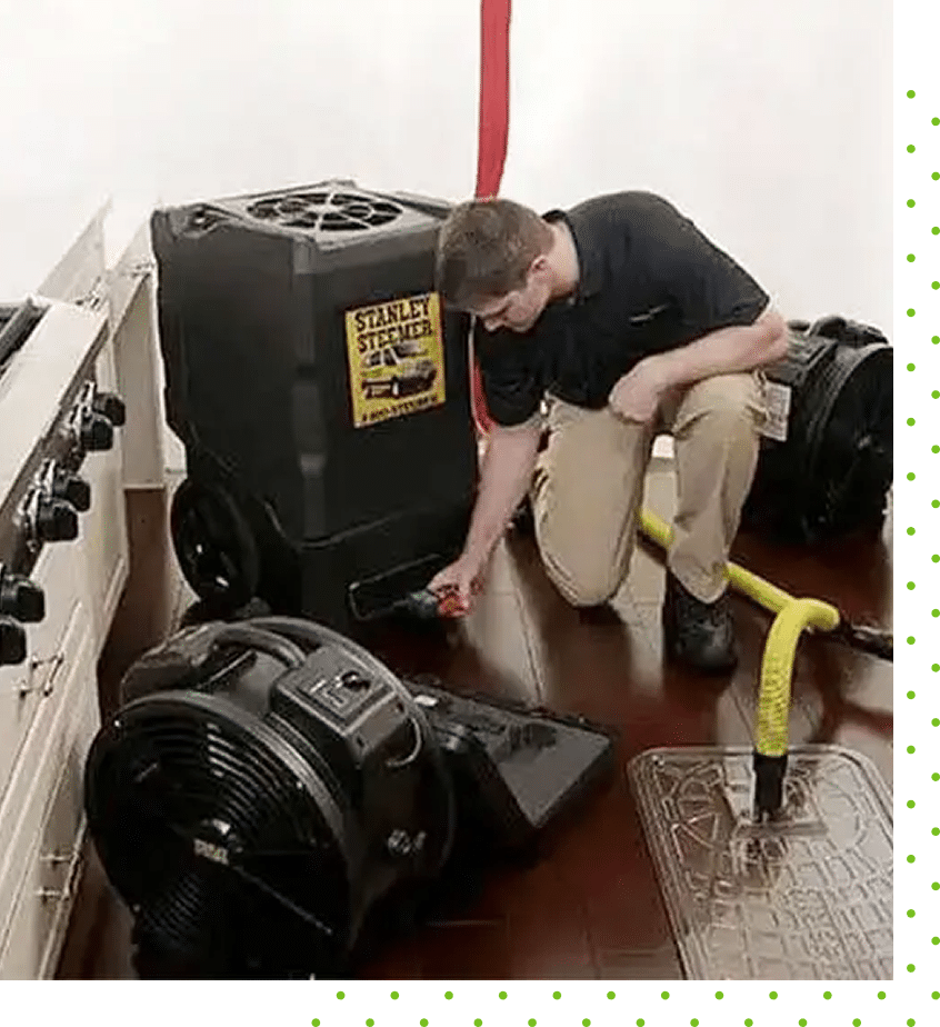 Technician using Stanley Steemer drying and dehumidifier equipment for water damage cleanup on a hardwood floor in a kitchen.